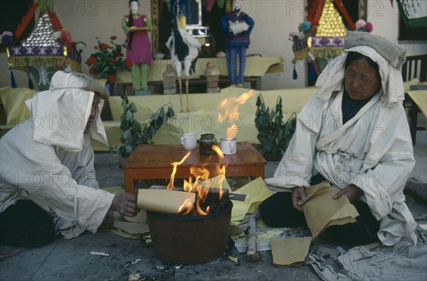 CHINA, Gansu Province, Symbolic paper money burnt at Taoist funeral with close relatives wearing white shrouds to indicate mourning.