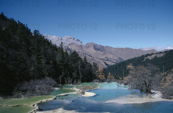 CHINA, Sichuan Province, Huanglong, View across pools formed by calcium carbonate in water towards green forest and mountains