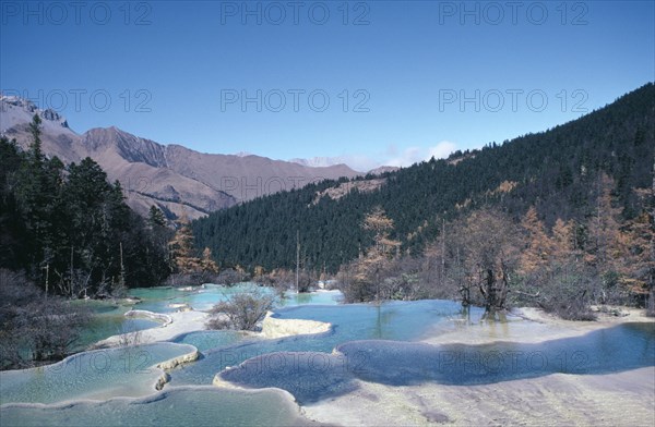 CHINA, Sichuan Province, Huanglong, View across pools formed by calcium carbonate in water towards green forest and mountains