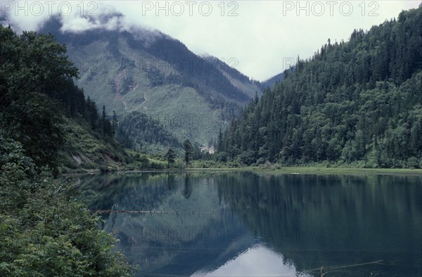 CHINA, Sichuan Province, Huanglong, Jiuzhaigou Nature Reserve. Lake surrounded by green tree covered mountains with reflections on water