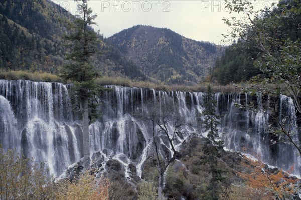 CHINA, Sichuan Province, Huanglong, Jiuzhaigou Nature Reserve multi level waterfalls with tree covered mountains behind