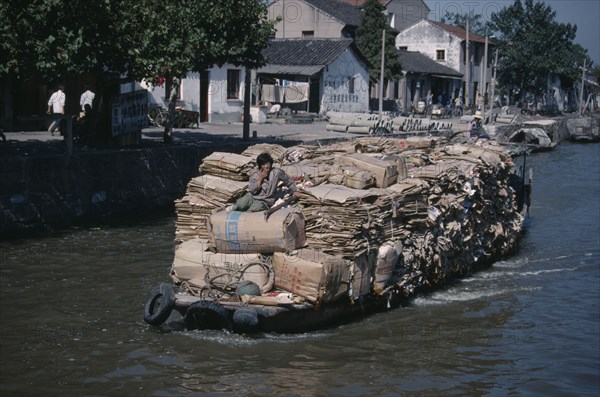 CHINA, Jiangsu Province, Suzhou, Man on boat travelling along the Grand Canal carrying piles of cardboard between Suzhou to wuxi