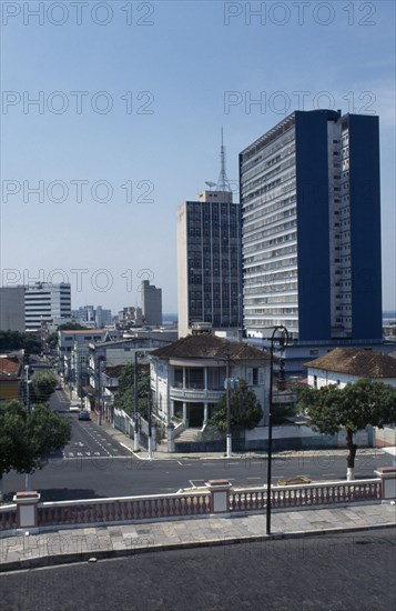 BRAZIL, Amazonas, Manaus, Downtown area. View across a road towards a street of houses with high rise buildings behind