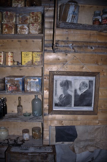 ANTARCTICA, Ross Sea, Ross Island, Cape Royds. Interior of Shackletons Hut built in 1908 with framed photographs on the wall and shelves with rusty tinned food containers