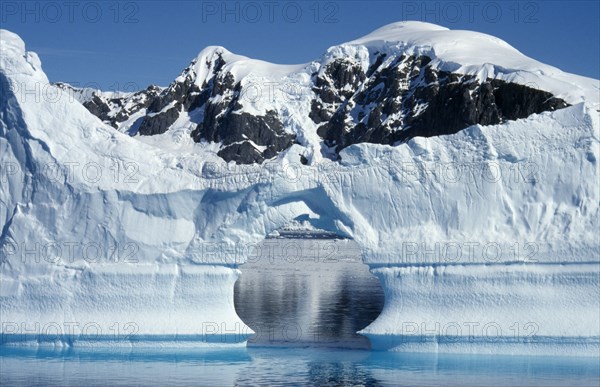 ANTARCTICA, Peninsula Region, Ice Cliffs with an arch shaped gap in the middle and snow covered mountains behind