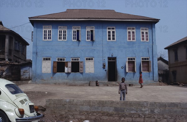 NIGERIA, Inagbiji, Blue painted exterior of typical house with wooden shutters and children in yard outside.