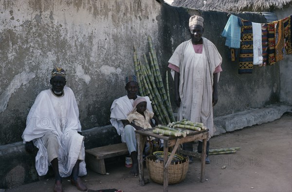 NIGERIA, Plateau, Three traditionally dressed men with little girl selling sugar cane from roadside stall.
