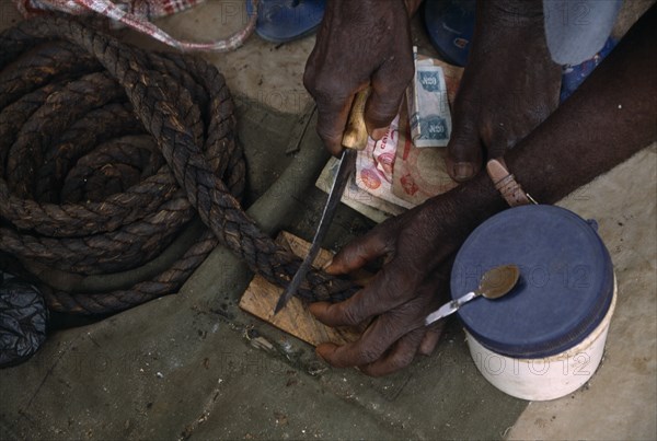 NIGERIA, Benue, Cropped shot of vendor cutting piece of tobacco at stall.