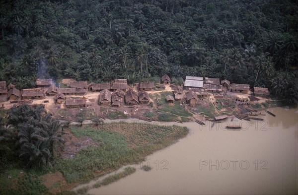 NIGERIA, Rivers State, Aerial view over thatched village on river bank beside area of tropical forest.