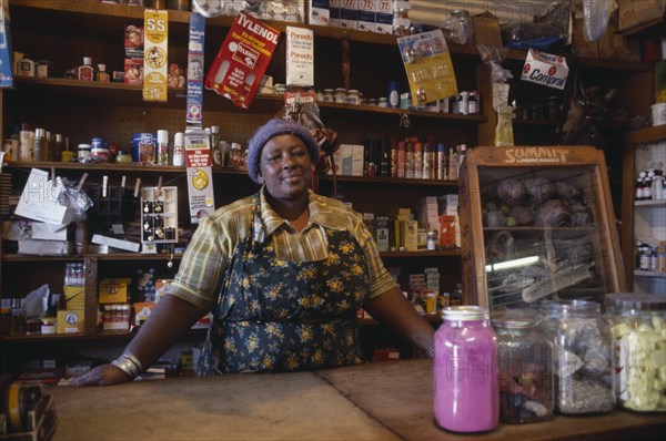 SOUTH AFRICA, Gauteng, Soweto, Portrait of shopkeeper behind counter with goods arranged on shelves behind her.