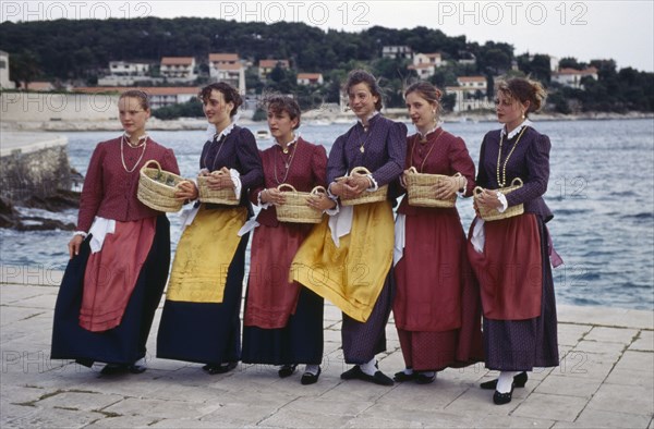 CROATIA, Dalmatia, Hvar Island, Girls in traditional clothing holding baskets greeting arriving visitors