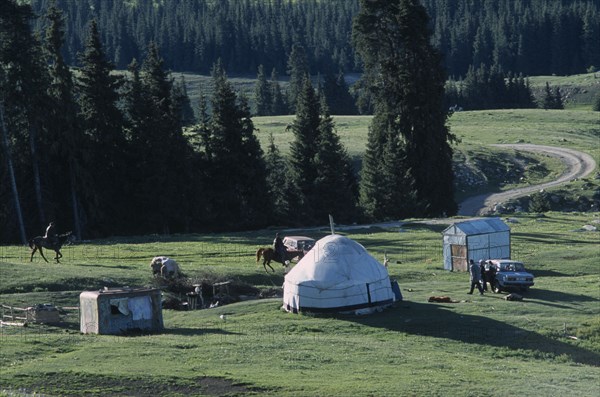 KIRGHIZSTAN, Tyan Shan, "Two men on horses, some standing around a car next to a yurt and small sheds."