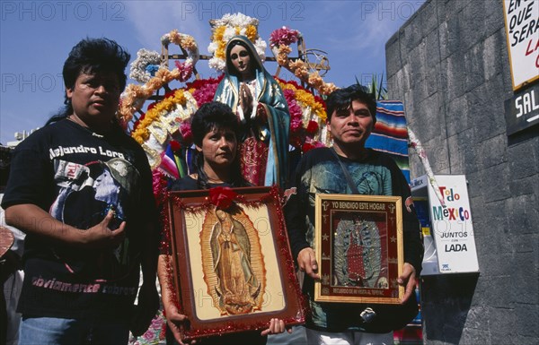 MEXICO, Mexico City, Pilgrims carrying icons and standing in front of statue of the Virgin Mary decorated with flowers at the Basilica de Guadeloupe for Day of Our Lady of Guadeloupe festival.
