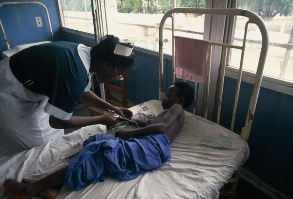 GHANA, Accra, Bedridden child being attended by nurse in children’s ward of Korle-Bu teaching hospital.