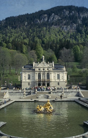 GERMANY, Bayern, Schloss Linderhof, Palace exterior with tourists crowds gathered at entrance.  Ornamental lake with gold statue in the foreground.  Smallest of three castles built by King Ludwig II.