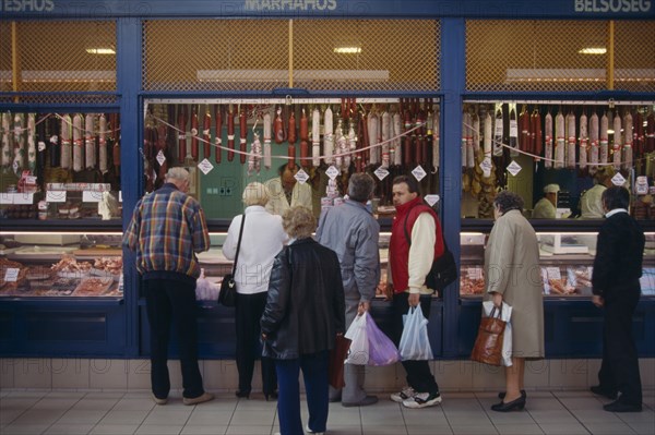 HUNGARY, Budapest, Tourists buying salami from butchers with counter open on to street.