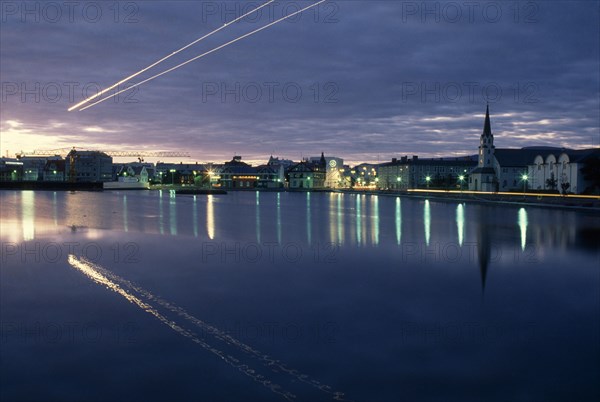 ICELAND, Reykjavik, The Tjörn or lake in city centre at night with light from street lamps reflected across flat surface.