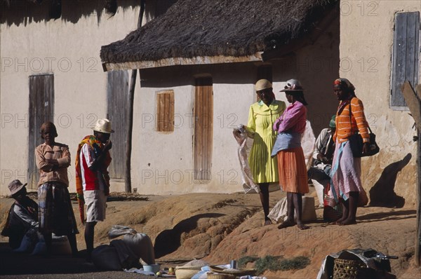 MADAGASCAR, People, Road to Ranomafana. Malagasy local people wearing traditional colourful clothing standing outside thatched housing in a village