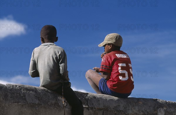 MADAGASCAR, Fianarantsoa, Two boys sitting on a wall one wearing a red baseball shirt and cap