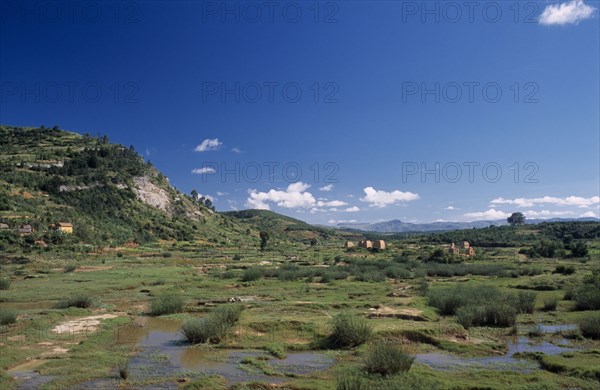 MADAGASCAR, Landscape, Road to Ambalavao. View across green flood plain  towards clay brick kilns and tree covered hills
