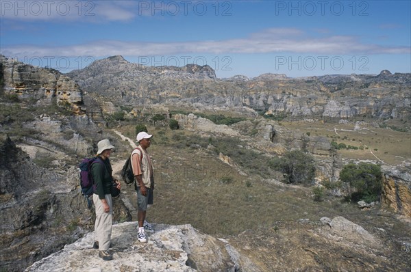 MADAGASCAR, Isalo National Park, Tourist and guide standing on edge of rock looking over craggy sandstone massifs