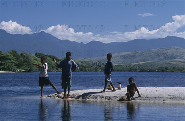 MADAGASCAR, Fort Dauphin, Lokaro, Group of children with a small dog fishing in the bay and mountains seen across water