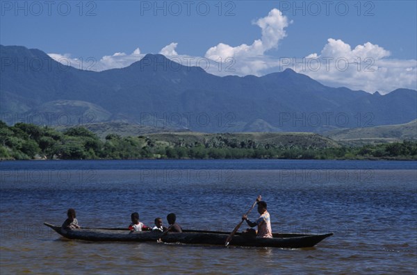 MADAGASCAR, Fort Dauphin, Lokaro, Mother ferrying her children across the bay in a Pirogue with mountains in the distance