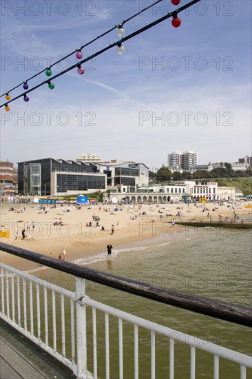 ENGLAND, Dorset, Bournemouth, The East Beach from the pier with seafront restaurants and bars. Adults and children play in the sand on the beach and at the water's edge between the groynes. Hotels and flats line the clifftop into the distance Paul Seheult