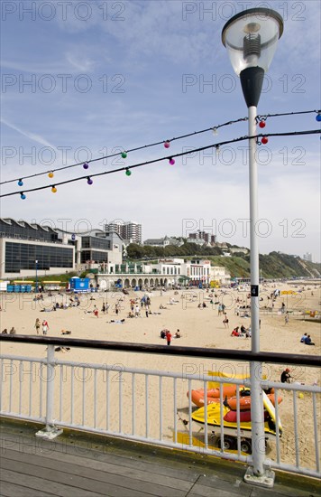 ENGLAND, Dorset, Bournemouth, The East Beach from the pier with seafront restaurants and bars. Adults and children play in the sand on the beach and at the water's edge. Hotels and flats line the clifftop into the distance