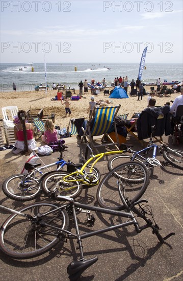 ENGLAND, Dorset, Bournemouth, Tourists watching speedboat races off the West Beach and playing in the sand. Mountain bikes lie on the promenade