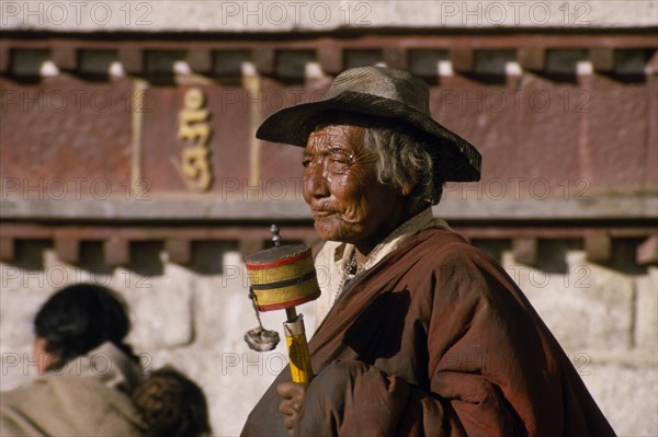 CHINA, Tibet, Lhasa, An elderly pilgrim with prayer wheel in the Barkhor Bazaar