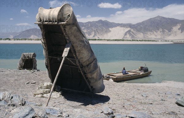 CHINA, Tibet, "Near Tsetang. Yak skin boats, one propped up by a paddle, and a local ferry beside the Yarlung Tsangpo, Brahmaputra River."