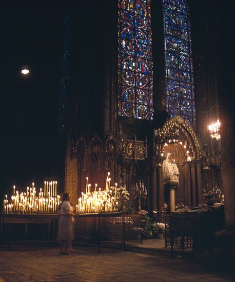 FRANCE, Central Loire, Chartres, Interior of cathedral showing Notre Dame du Pillar black Madonna beneath stained glass window and women lighting candles.
