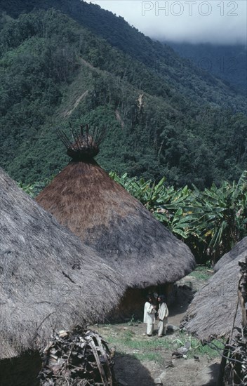 COLOMBIA, Sierra Nevada de Santa Marta, Chendukua, "Old traditional centre of Chendukua Two mamas/priests talk and ceremonially greet each other by exchanging coca leaves, outside old nuhue/temple with conical thatched roof & sacred potsherds in rack at apex. Bananas and plantains grown close to village yucca/manioc and maize on cleared hillside behind. Kogi Tribe "