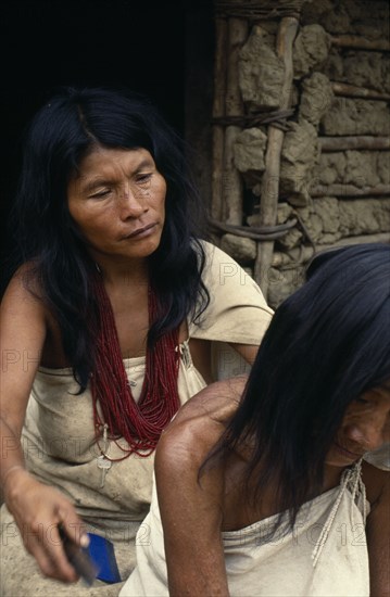 COLOMBIA, Sierra Nevada de Santa Marta, Sierra Avingue, Parque Nacional. Kogi mother and grandmother sit outside family home in Avingue  Mother combs head lice out of old grandma's hair. She wears many strands of dark red glass beads  the favourite colour of Kogi women and a sign of great wealth