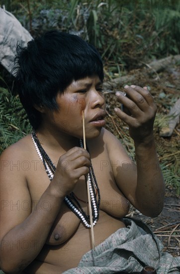 COLOMBIA, Sierra de Perija, Yuko - Motilon ., "Woman applying red “Achiote” facial paint extracted from ground Achiote seeds, using a trade mirror and wearing traded plastic beads"