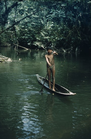 COLOMBIA, Choco Region, Noanama Tribe, Boy paddles canoe along tributary stream through dense tropical jungle. Wearing intricately made silver earplugs as adornment – to attract girls
