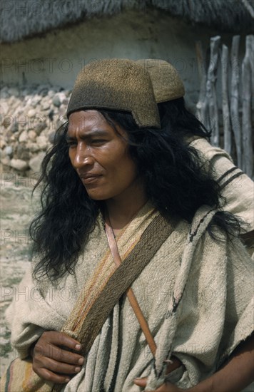 COLOMBIA, Sierra Nevada de Santa Marta, Ika Tribe, "Nabusimaque village administrative centre.  Two Ika men, one only partly seen, dressed in traditional woven clothes with typical “fique” / cactus fibre helmets and “mochilas” / shoulder bags"