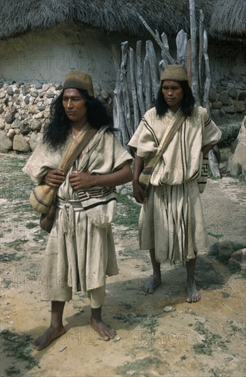 COLOMBIA, Sierra Nevada de Santa Marta, Ika Tribe, "Nabusimaque village.  Two Ika men in traditional woven mantas / cloaks, with “fique” / cactus fibre helmets and woven wool “mochilas” / shoulder bags with Ika designs"