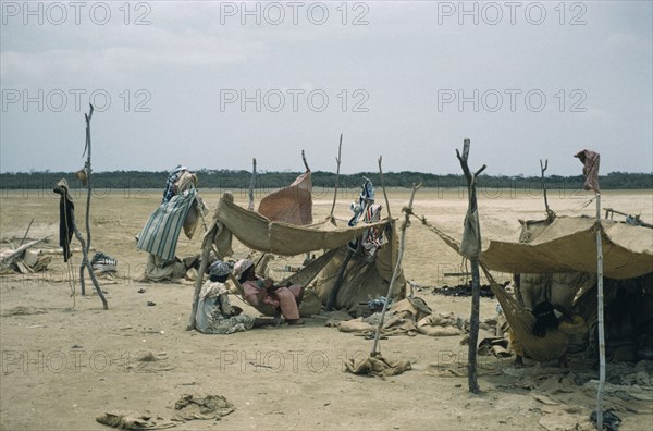 COLOMBIA, Guajira Peninsula, Guajiro / Wayuu Tribe, Portete a coastal desert settlement.  Wayuu encampment consisting of shelters of hardwood poles and old sacks. Women sewing inside central shelter.