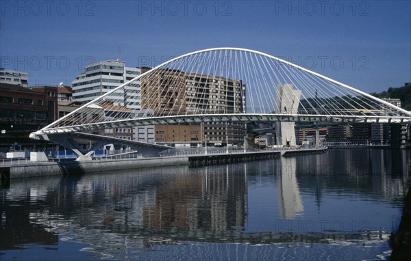 SPAIN, Basque Country, Bilbao, Campo Volantin footbridge over the River Nevion near the Guggenheim with high rise apartment buildings behind reflected in water below.