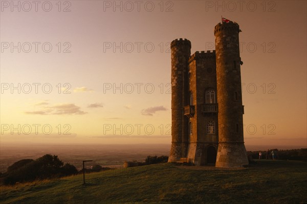 ENGLAND, Worcestershire , Broadway Tower seen in golden light with people standing on grass in the grounds behind tower
