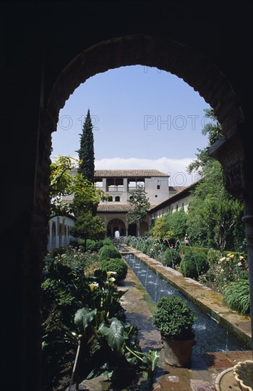SPAIN, Andalucia, Granada, The Generalife.  Long central pool in the Patio de la Acequia enclosed oriental garden framed by archway.