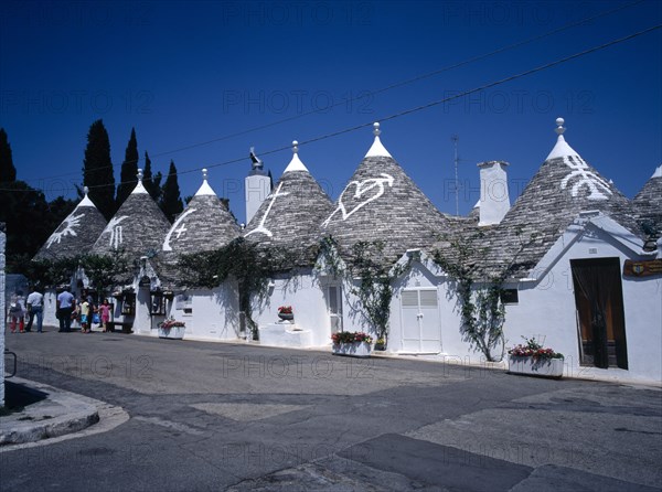 ITALY, Puglia, Bari Provence, "White Trulli buildings with runic symbols painted on the grey stone roofs in Alberobello village that have been converted into houses and a shop. No mortar is used, although the interior is plastered."
