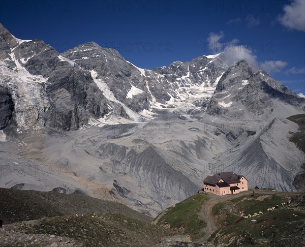 ITALY, Dolomites, Trentino, Sulden. A single pink building at the foot of Schaubachhutte with Mount Zebru and Ortler