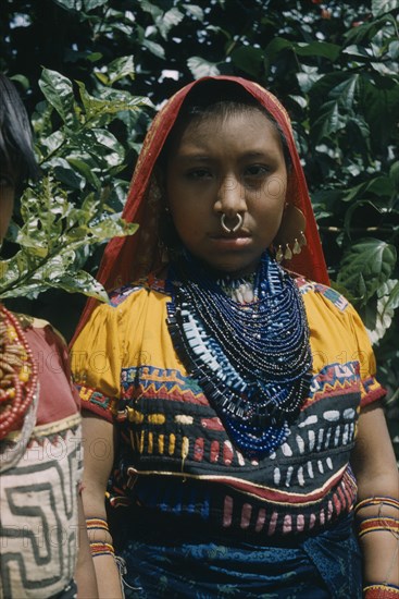 COLOMBIA, Arquia, Cuna Tribe, "Girl wearing glass bead necklace and typical bead amulets. She also wears a typical appliqué “mola” / blouse, a gold nose ring and gold and silver ear rings – signs of considerable wealth. Gulf of Darien, Arquia, close to Panamanian border."