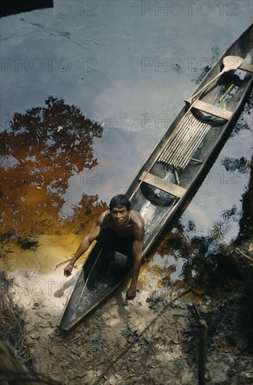 COLOMBIA, Vaupes Region, Tukano Tribe, Man beaches his canoe at a river port; note fishing rod and typically shaped Amazonian paddle.