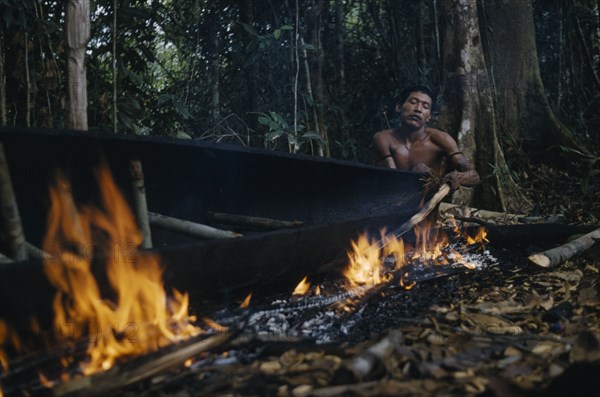 COLOMBIA, Vaupes Region, Tukano Tribe, Man warps open and stretches the sides of the canoe with wedges during the burning process.