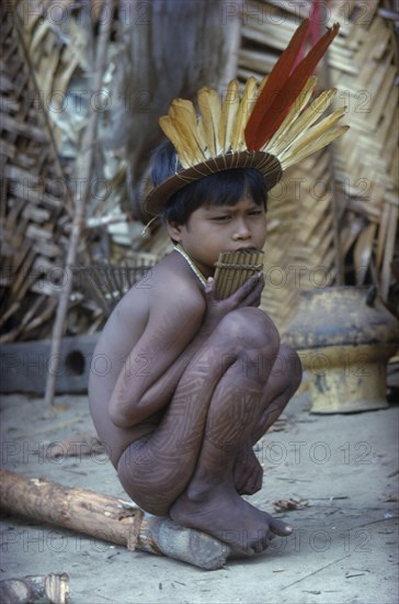 COLOMBIA, Vaupes Region, Tukano Tribe, "Young boy with “we” dark purple leaf dye and a crown of macaw and toucan feathers, plays the “carizu” panpipes"