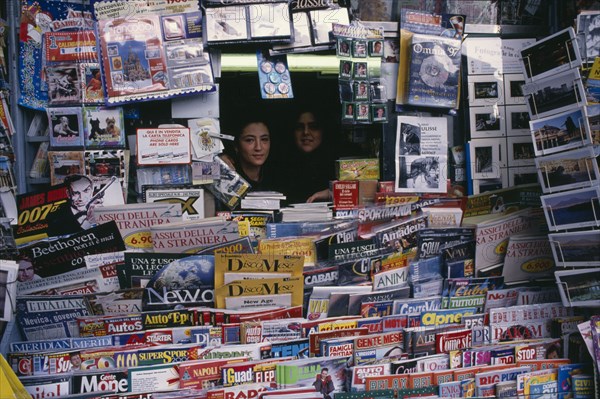 ITALY, Campania, Naples, Two women looking out from newsagents stall completely surrounded by newspapers and magazines.
